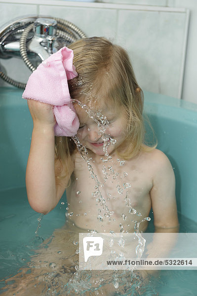 Mädchen  3 Jahre  wäscht sich mit einem Badelappen in der Badewanne