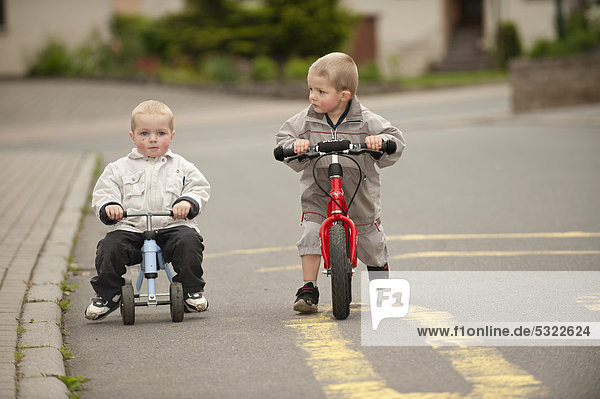 Zwei Jungen  4 und 3 Jahre  fahren mit Laufrad und Pukybike auf der Straße