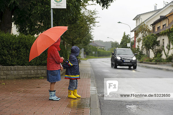 Zwei Kinder  3 und 7 Jahre  wollen im Regen die Straße überqueren  ein Auto kommt  Assamstadt  Baden-Württemberg  Deutschland  Europa