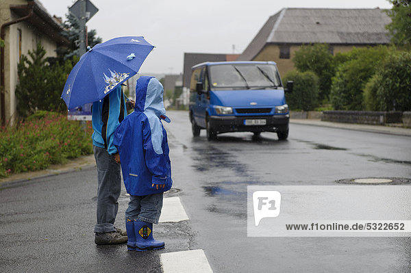 Zwei Kinder  4 und 8 Jahre  wollen im Regen die Straße überqueren  ein Auto kommt  Assamstadt  Baden-Württemberg  Deutschland  Europa
