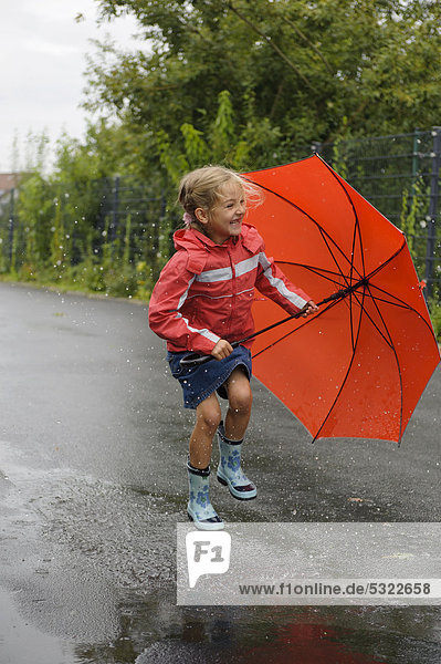 7jähriges Mädchen springt mit Regenschirm im Regen durch eine Pfütze auf der Straße  Assamstadt  Baden-Württemberg  Deutschland  Europa