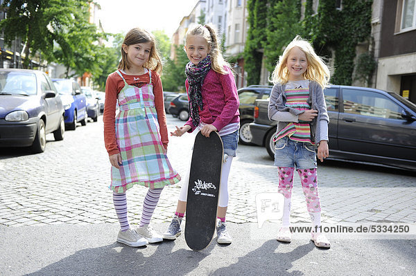 Drei Mädchen mit einem Skateboard auf einer Wohnstraße mitten in Düsseldorf  Nordrhein-Westfalen  Deutschland  Europa