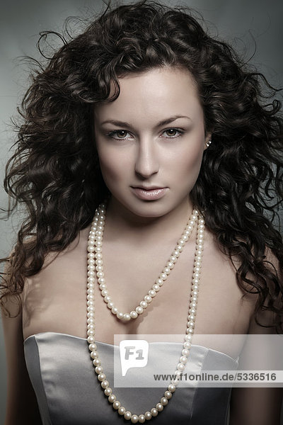 Junge Frau mit braunen Locken und Perlenkette  Beautyportrait