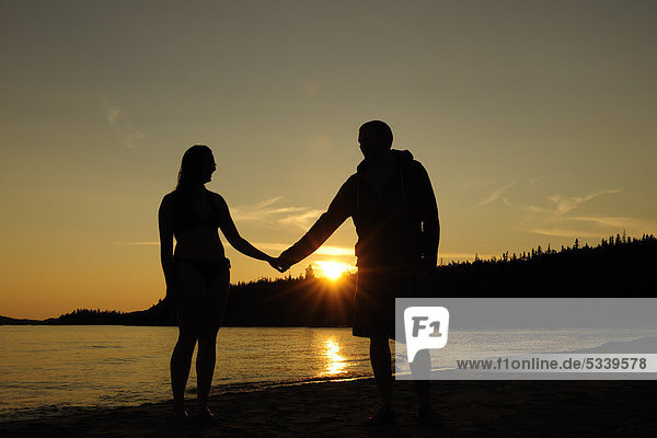 Pärchen steht händchenhaltend am Ufer des Lake Superior im Sonnenuntergang  Ontario  Kanada