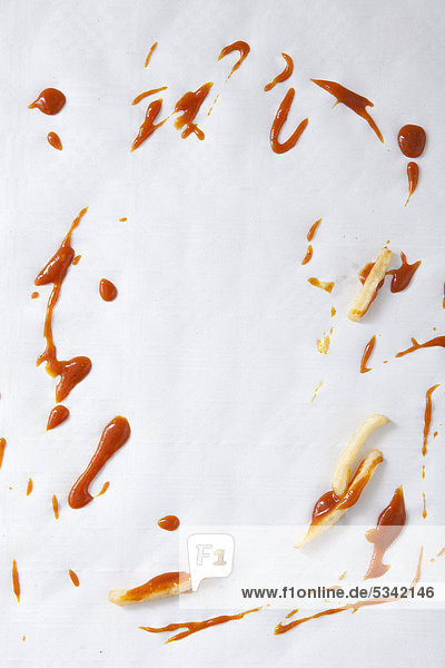 French fries and spilled ketchup on a paper table cloth  food scraps