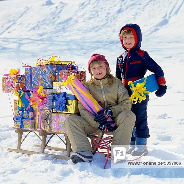 Children with Christmas presents on sledge in snow