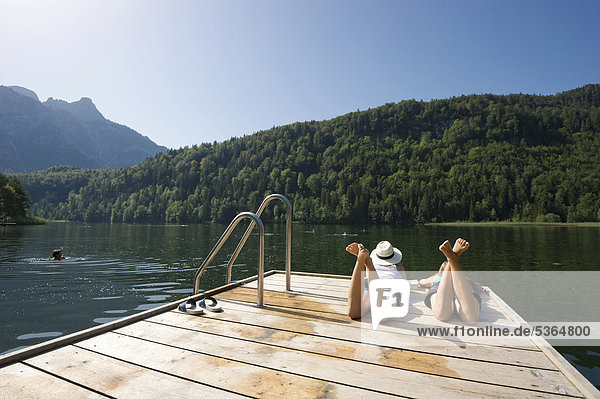 Young women lying on a landing stage on Lake Schwansee near Fuessen  Allgaeu region  Bavaria  Germany  Europe