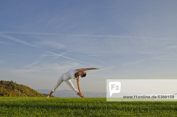 Junge Frau praktiziert Hatha-Yoga im Freien  zeigt die Stellung trikonasana  Dreieck  Nove Mesto  Okres Teplice  Tschechische Republik  Europa