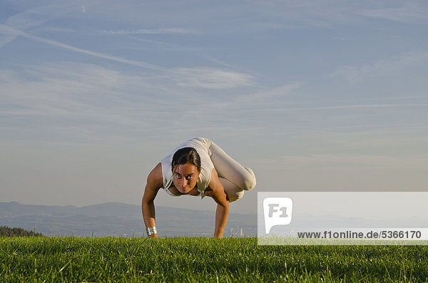 Junge Frau praktiziert Hatha-Yoga im Freien  zeigt die Stellung parshva kakasana  parshva bakasana  seitliche Krähe  seitlicher Kranich  Nove Mesto  Okres Teplice  Tschechische Republik  Europa