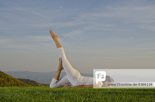 Junge Frau praktiziert Hatha-Yoga im Freien  zeigt die Stellung ardha shalabhasana  halbe Heuschrecke  Nove Mesto  Okres Teplice  Tschechische Republik  Europa