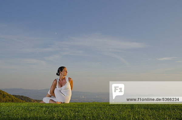 Junge Frau praktiziert Hatha-Yoga im Freien  zeigt die Stellung ardha matsyendrasana  halber Drehsitz  Nove Mesto  Okres Teplice  Tschechische Republik  Europa