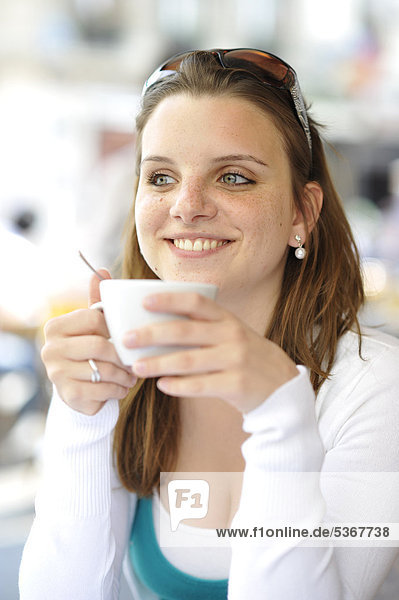 Junge Frau trinkt Kaffee  hält Kaffeetasse  in CafÈ  Paris  Frankreich  Europa