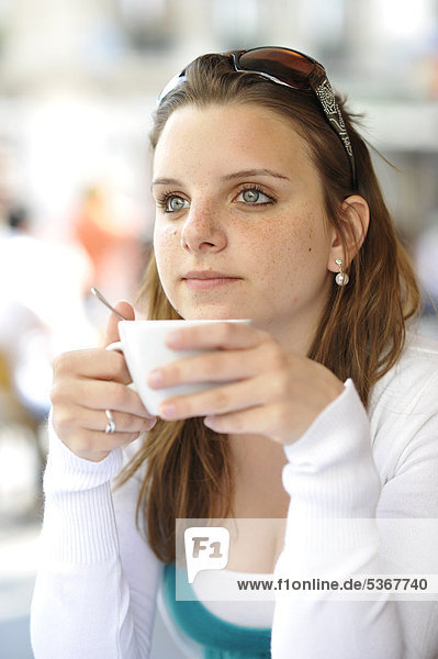 Junge Frau trinkt Kaffee  hält Kaffeetasse  in CafÈ  Paris  Frankreich  Europa