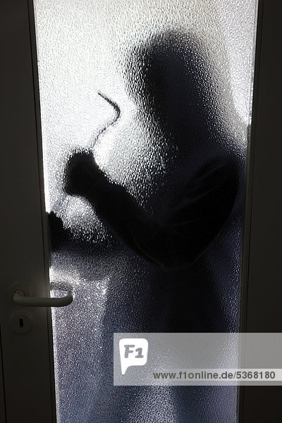 Einbruch  Wohnungseinbruch  Einbrecher tagsüber im Treppenhaus eines Mehrfamilienhauses bricht eine Glastür auf