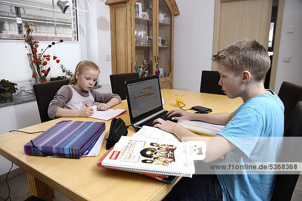 Geschwister machen im Wohnzimmer gemeinsam Hausaufgaben  Junge arbeitet mit einem Laptop Computer
