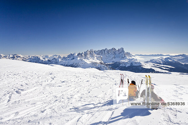 Skitourengeher machen Rast auf dem Gipfel vom Uribrutto oberhalb vom Passo Valles  hinten die Pallagruppe und der Passo Rolle  Trentino  Dolomiten  Italien  Europa