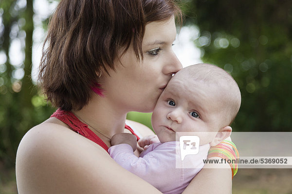 Junge Mutter umarmt und küsst ihr drei Monate altes Baby