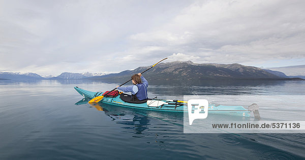 Woman in a sea kayak  paddling  sea kayaking  mountains behind  Tagish Highland  Atlin Lake  British Columbia  Canada  America