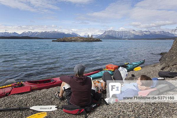 Two young women relaxing on the shore of Atlin Lake  sea kayaks  British Columbia  Canada  America