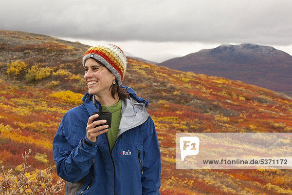 Young woman  hiker resting holding a cup  subalpine tundra  Indian summer  autumn  near Fish Lake  Yukon Territory  Canada