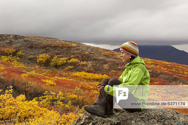 Young woman sitting on a rock  resting  enjoying view  subalpine tundra  Indian summer  autumn  near Fish Lake  Yukon Territory  Canada