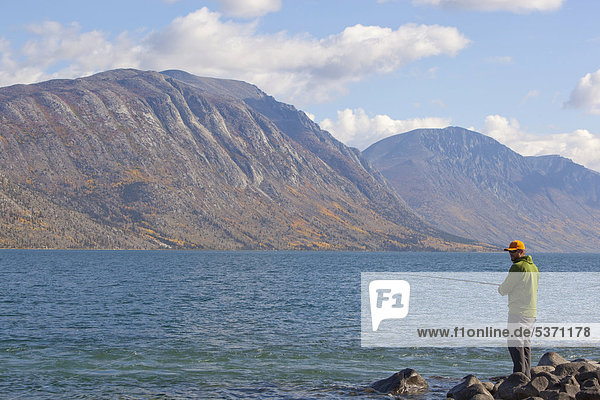 Man spin fishing  Kusawa Lake  mountains behind  Indian summer  autumn  Yukon Territory  Canada