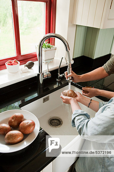 Mutter und Sohn waschen Kartoffeln in Küchenspüle