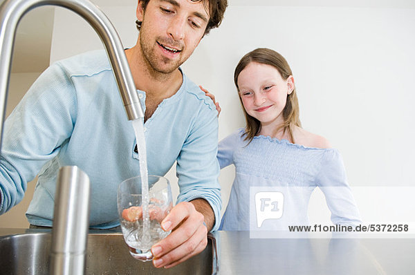 Junger Mann füllt ein Glas Wasser für Tochter