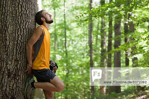 Man leaning against tree holding water bottle