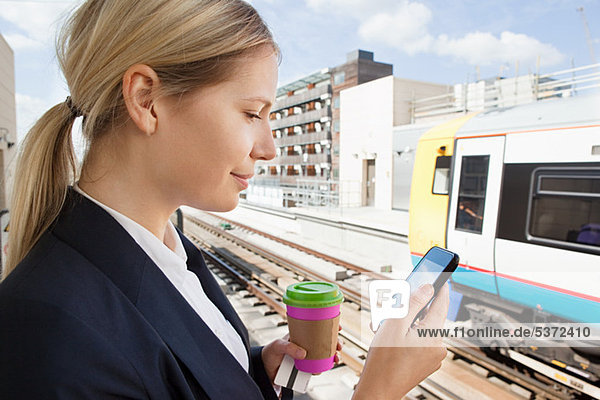 Geschäftsfrau mit Kaffee und Smartphone im Bahnhof