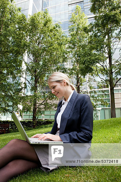 Geschäftsfrau auf Rasen sitzend und mit Laptop