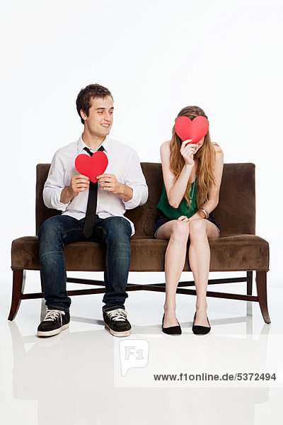 Junges Paar sitzend auf Sofa mit Herzformen auf weißem Hintergrund