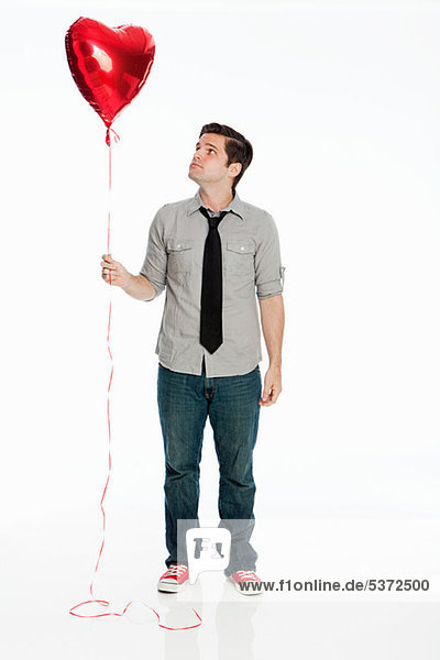 Junger Mann hält Ballon vor weißem Hintergrund
