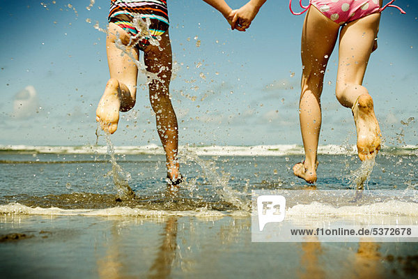 Two girls holding hands running into sea