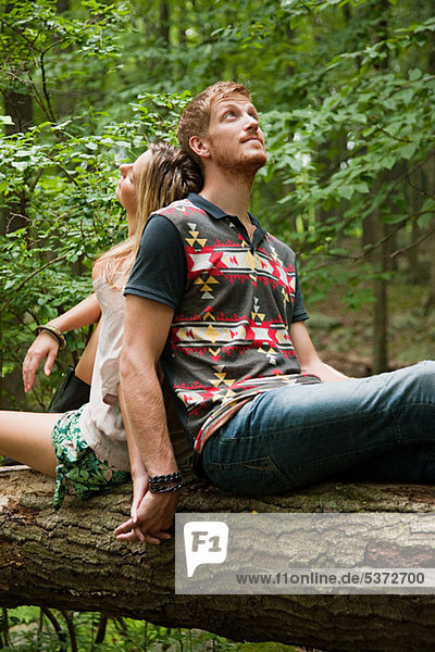 Couple leaning against each other on log in forest
