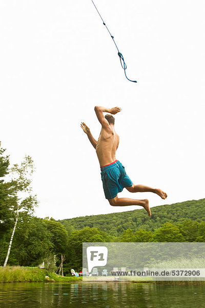 Teenage boy swinging off a rope into a lake