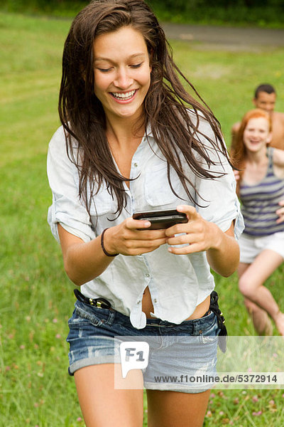 Teenage Girl looking at Handy während des Gehens in Landschaft mit Freunden