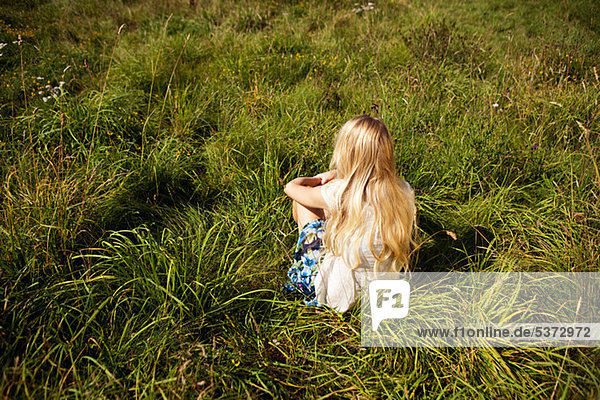 Junge Frau sitzt friedlich auf einem Feld.
