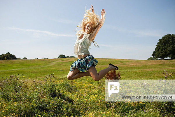 Junge Frau auf einem Feld  die in die Luft springt.