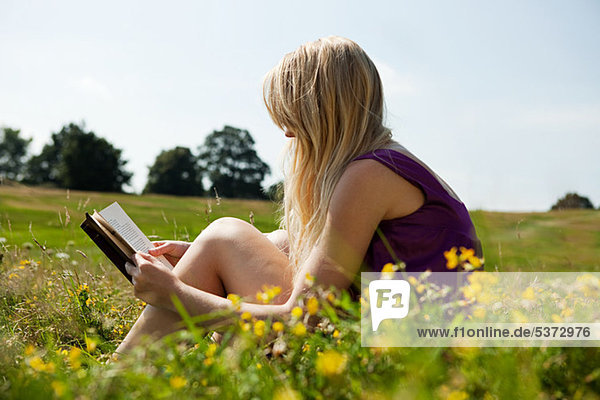 Junge Frau beim Lesen eines Buches auf einem Feld
