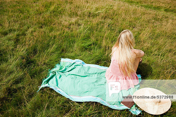Young Woman sitting on einen Schal in einem Feld