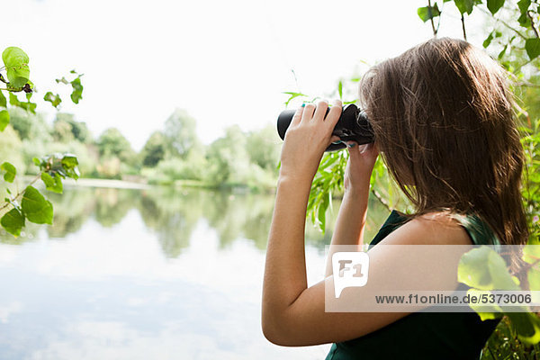 Junge Frau  die durch ein Fernglas über einen See schaut