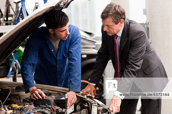 Businessman looking at car engine with mechanic