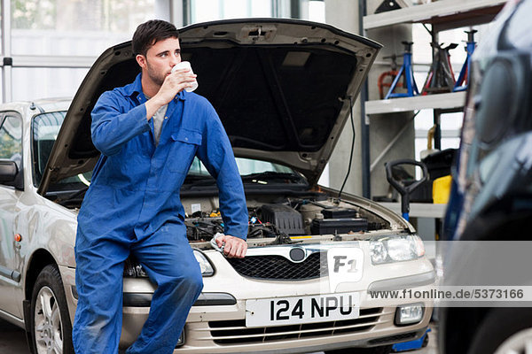 Young mechanic drinking coffee on car