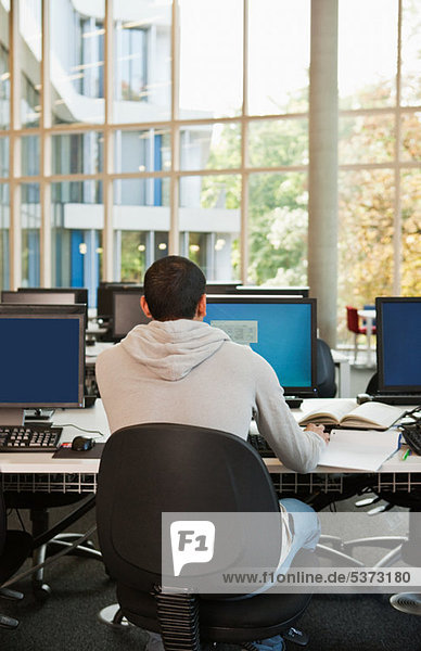 Universitätsstudent bei der Arbeit am Computertisch  Rückansicht