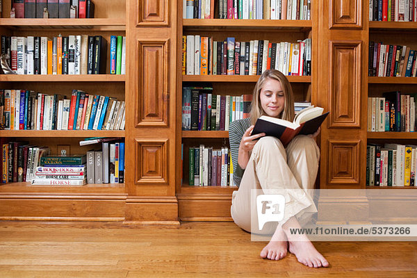 Young woman reading on floor by bookshelves