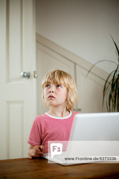 Boy looking up von Laptop auf Schreibtisch