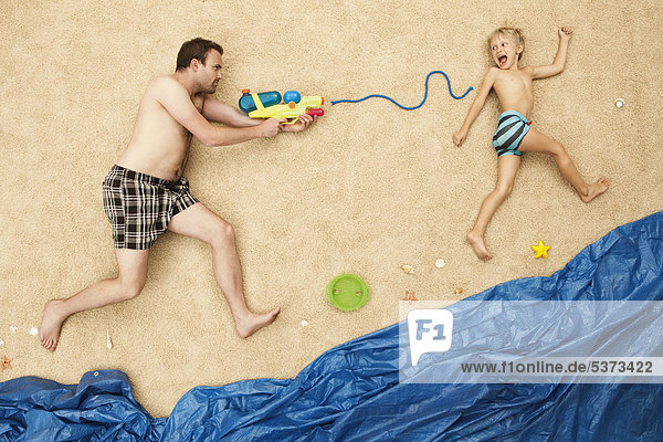 Deutschland  Vater und Sohn spielen mit Wasserpistolen am Strand