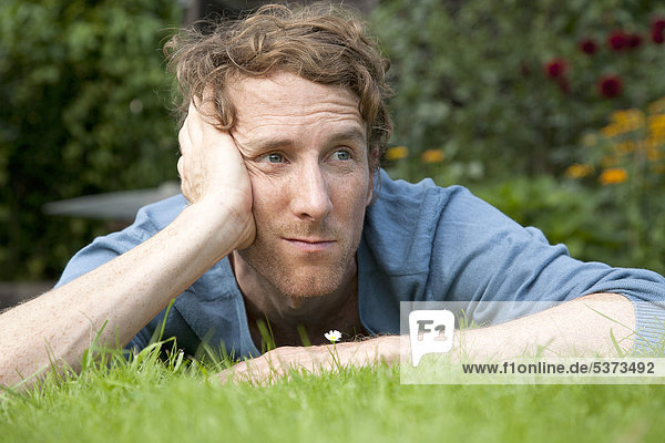 Mann denkt  während er auf Gras vor dem Gänseblümchen liegt.