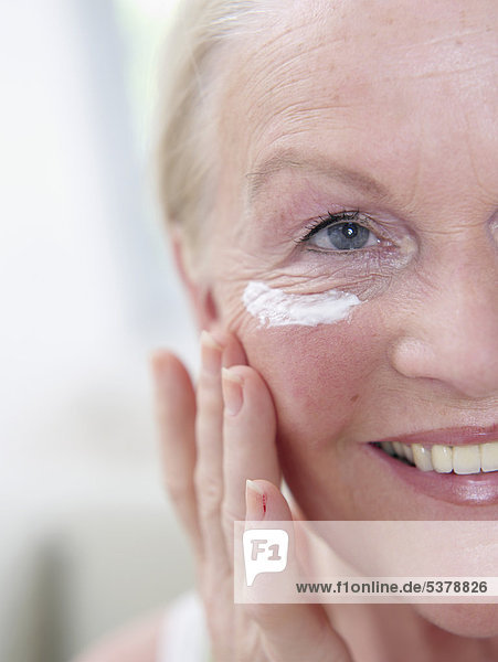Senior woman applying face cream on face  close up